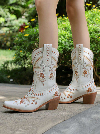 White cowboy boots with floral embroidery on a blurred outdoor background