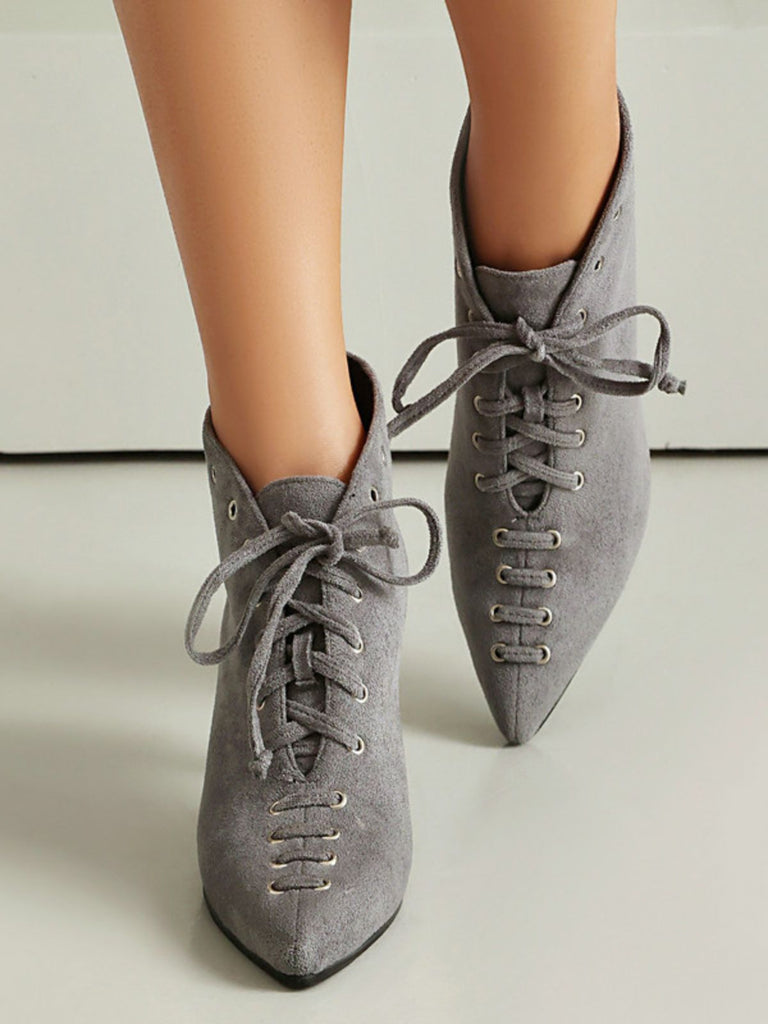 Gray suede pointed-toe shoes with laces on a neutral background