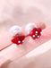 Pair of earrings with white pearls and red strawberry-shaped pendants on a hand.