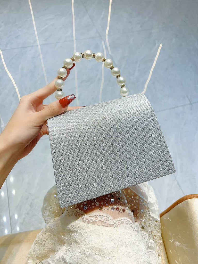 Silver clutch bag with pearl handle held by a hand against a light blue background