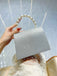 Silver clutch bag with pearl handle held by a hand against a light blue background