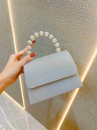 Hand holding a light blue handbag with pearl handle against a neutral background