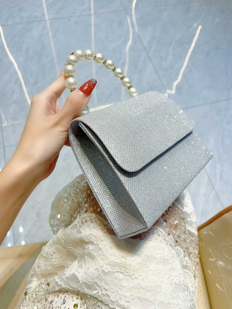 Silver clutch bag held by a hand with a pearl handle against a textured surface