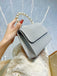 Silver clutch bag held by a hand with a pearl handle against a textured surface