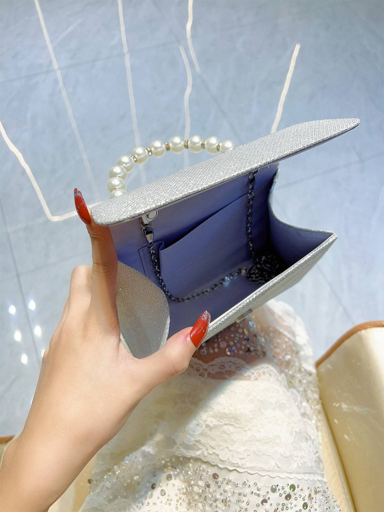 Hand holding a silver clutch with pearl handle against a light blue background