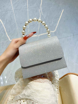 Silver clutch bag with pearl handle held by a hand against a light blue background