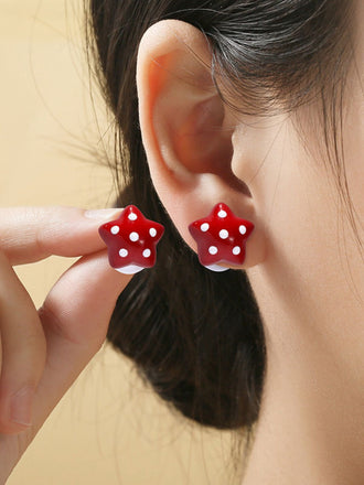 Close-up of a person wearing red star-shaped earrings with white dots.