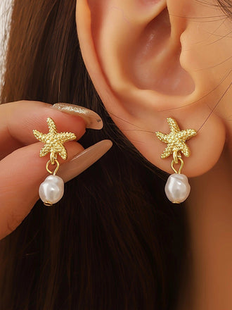 Gold starfish earrings with pearl drops worn by a person.