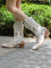 White embroidered cowboy boots on a person walking outdoors with greenery in the background
